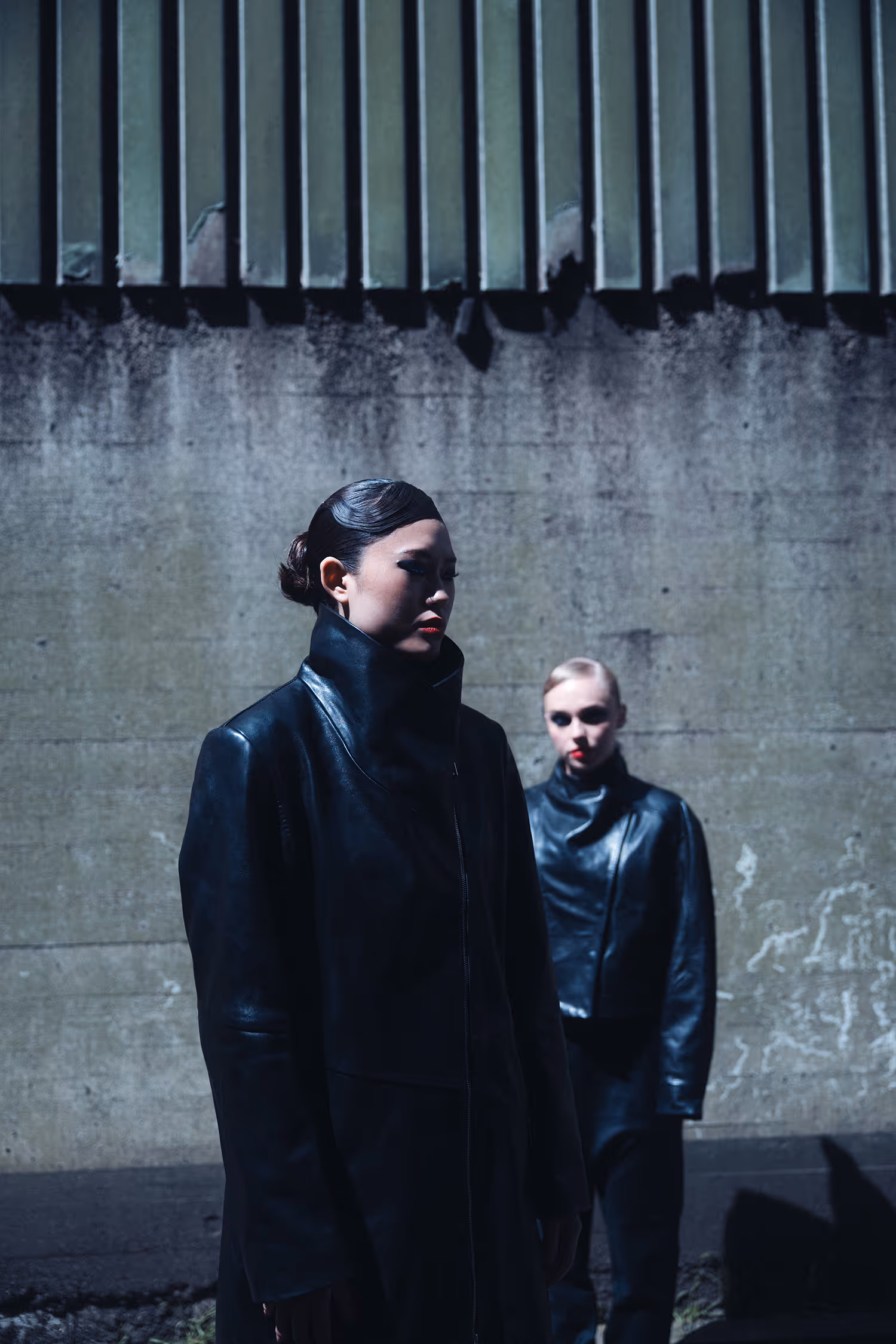 Two women dressed in black standing by the wall.