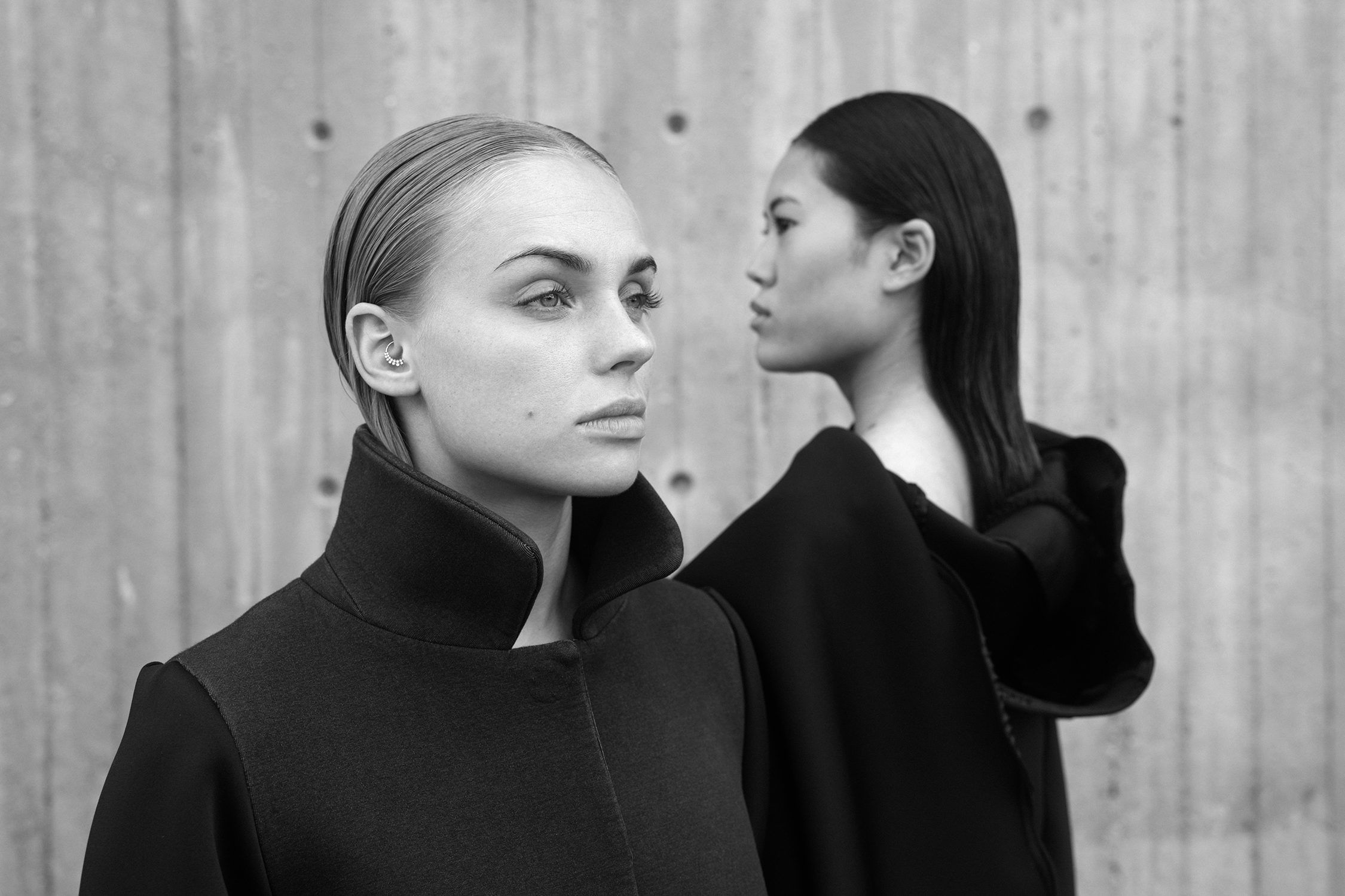 Two women standing by the wall each looking in a different direction