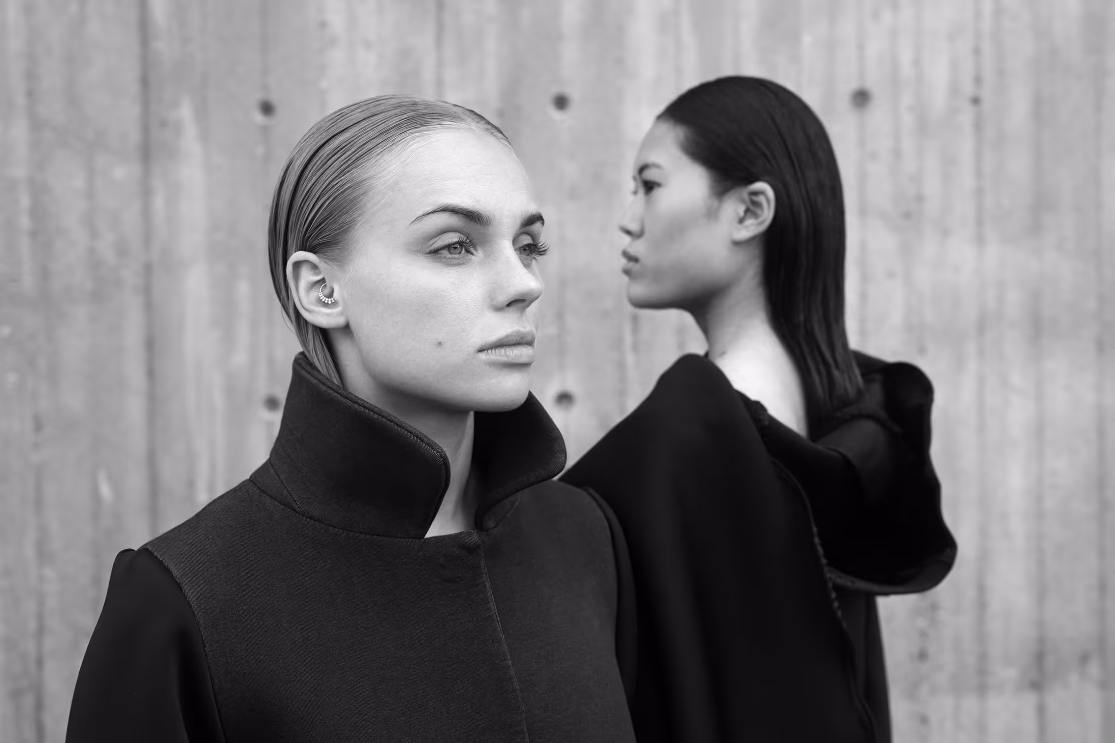 Two women standing by the wall each looking in a different direction