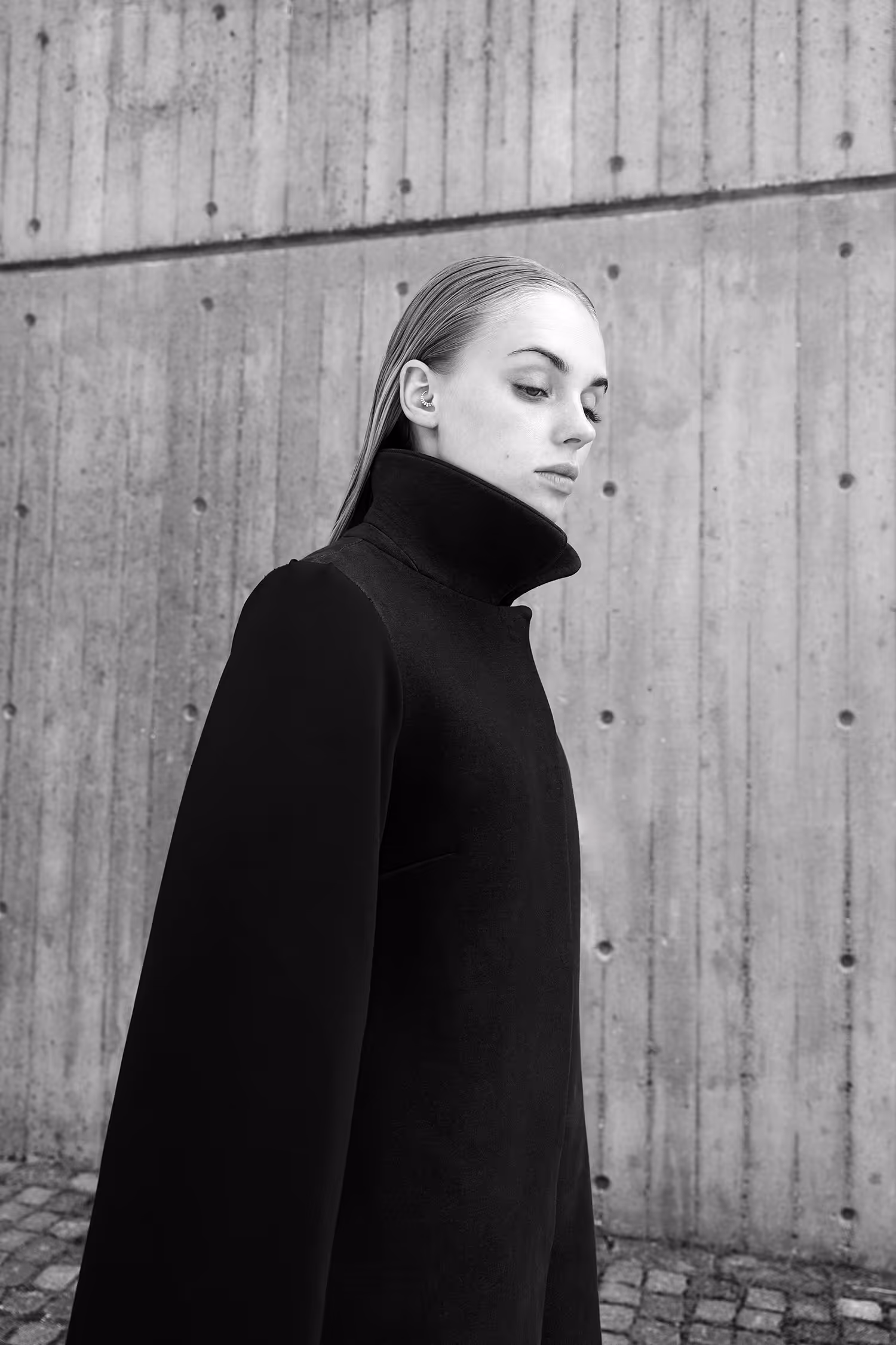 Woman in a black coat standing slightly sideways by the wall