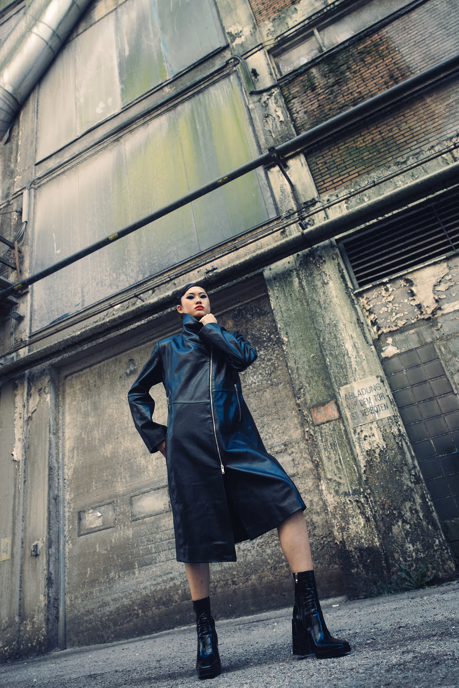 Woman in a leather coat with her hand by her chin standing by the wall