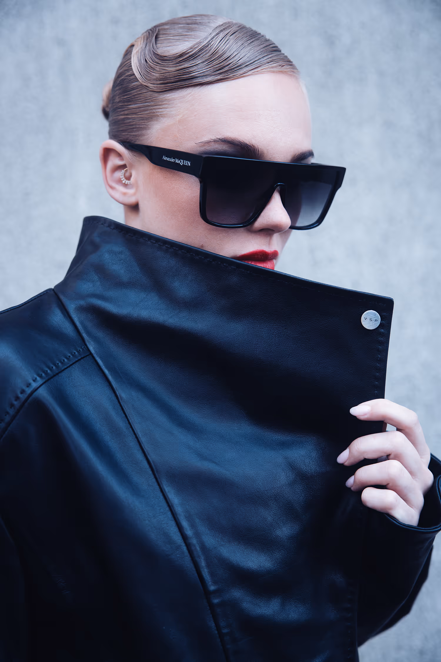 Woman in sunglasses covering her chin with the collar of a black leather jacket